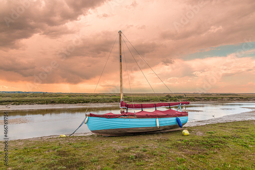 A sailing dinghy beside the River Glaven on the salt marshes at Blakeney National Nature Reserve at Blakeney, Norfolk UK photo