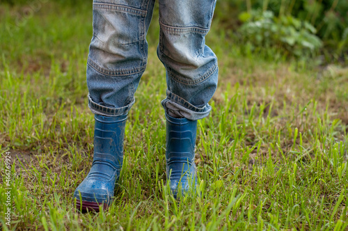 children's feet in dirty blue rubber boots and jeans stand on the grass