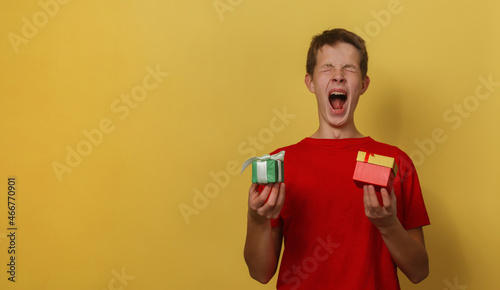 A 15 year old boy in a red T-shirt is holdA 15 year old boy in a red T-shirt is holding Christmas presents and screaming for joy with his eyes closed. © gelog67
