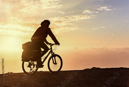 Mountain bicycle rider with backpack travels over sunrise background