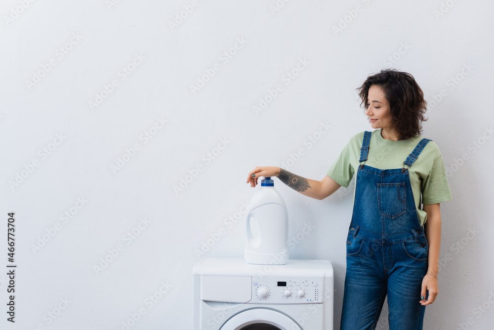 smiling housewife standing near bottle of detergent on washing machine. smiling housewife standing near bottle of detergent on washing machine.