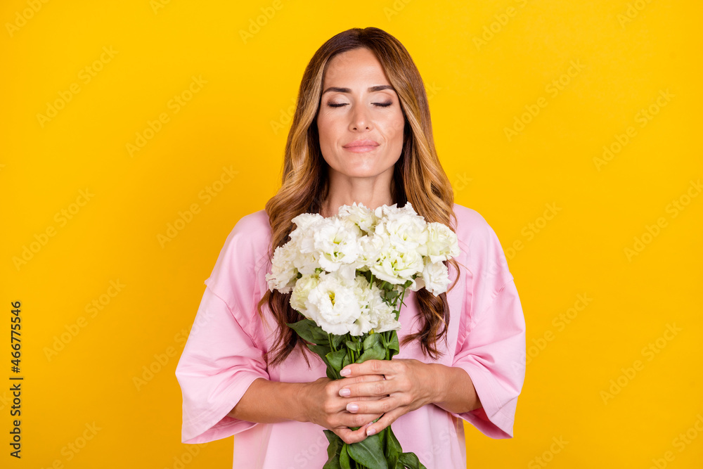Photo of young happy positive woman hold hands smell flowers smile enjoy isolated on yellow color background Photo of young happy positive woman hold hands smell flowers smile enjoy isolated on yellow color background