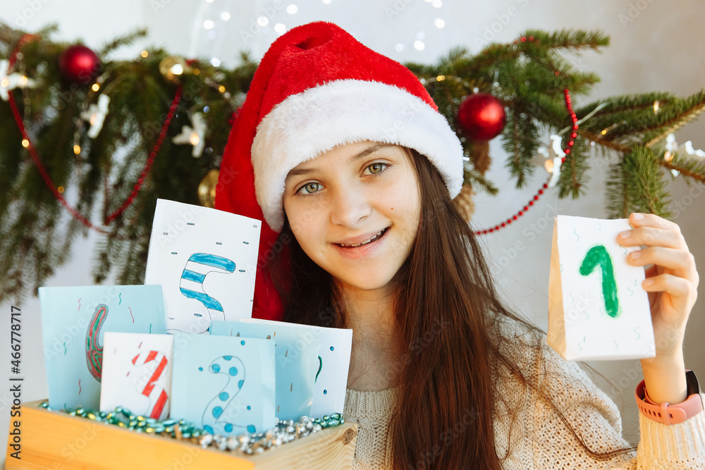 a happy girl in a Christmas hat holds an Advent calendar in her hands diy a happy girl in a Christmas hat holds an Advent calendar in her hands diy