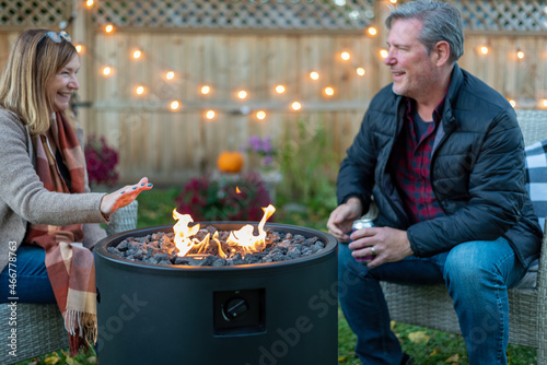 Middle age couple sitting by a backyard fire pit in autumn
