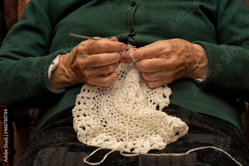 A 90-year-old lady crochets with white yarn