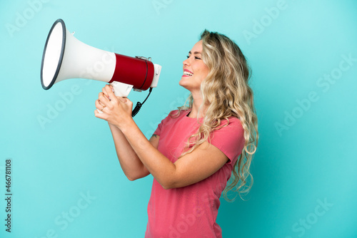 Young Brazilian woman isolated on blue background shouting through a megaphone to announce something