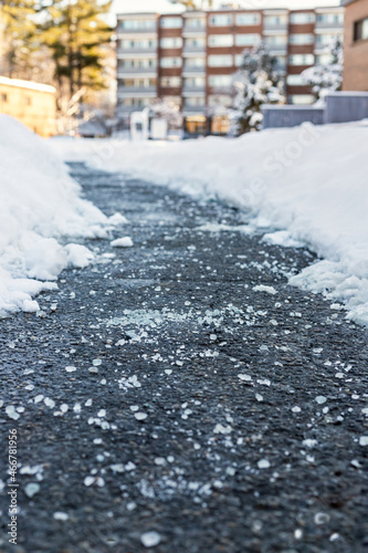 Winter road with salt for melting snow and apartment building in background. Selective focus