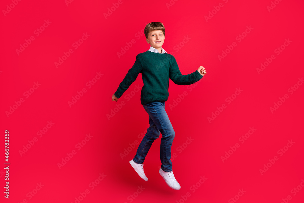 Photo of handsome sweet schoolboy dressed green sweater jumping high running smiling isolated red color background