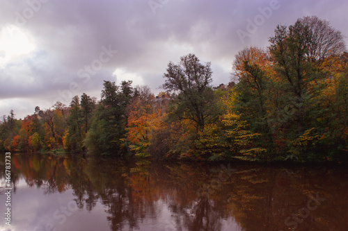 River lined with colorful trees in autumn, reflecting in the water. © Almossaid