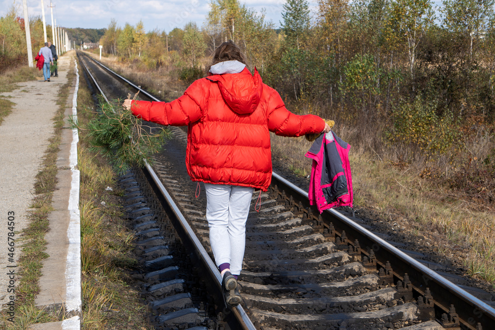Young caucasian woman with wavy hair in red jacket walking on the railroad in small village