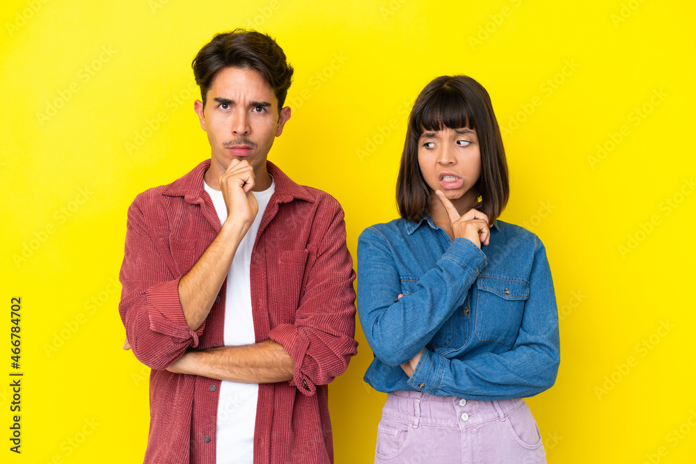 Young mixed race couple isolated on yellow background having doubts while looking up Young mixed race couple isolated on yellow background having doubts while looking up