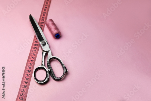 Spool of thread, centimeter and sewing scissors on a pastel pink background. Models for tailors or textile workshops. Empty space for text. photo