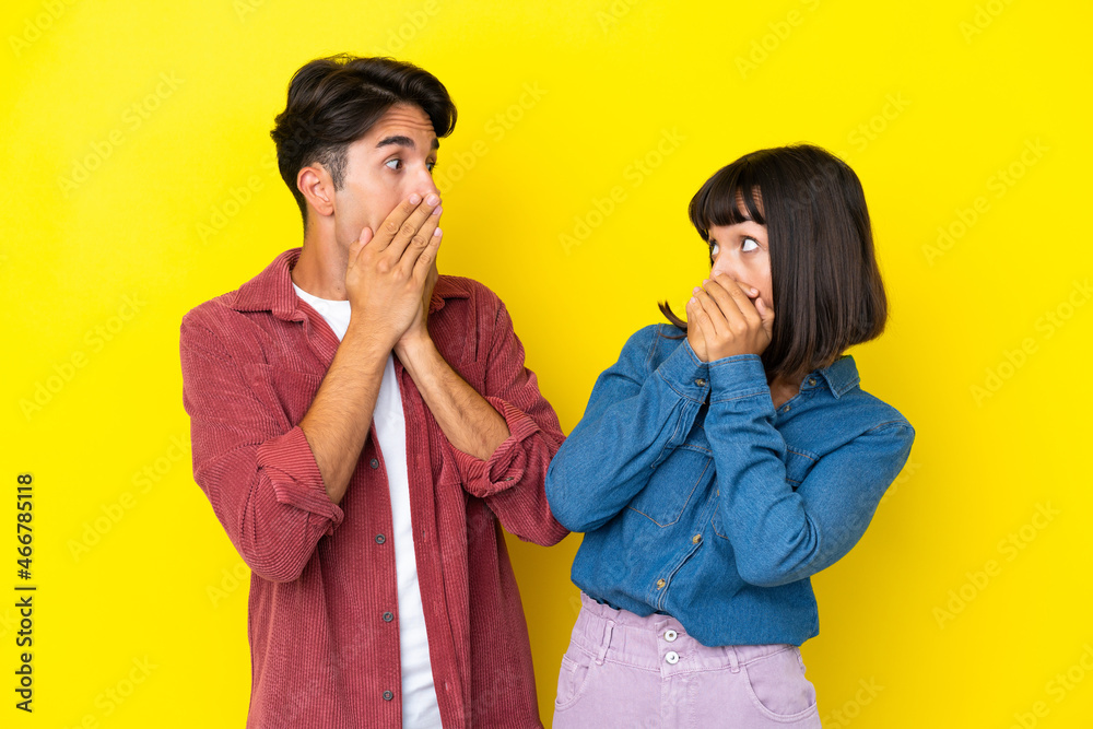 Young mixed race couple isolated on yellow background covering mouth with hands for saying something inappropriate Young mixed race couple isolated on yellow background covering mouth with hands for saying something inappropriate