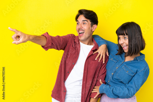 Young mixed race couple isolated on yellow background presenting an idea while looking smiling towards