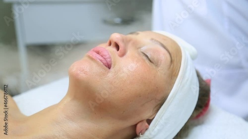 Facial peeling mask, spa beauty treatment, skin care. Woman getting facial treatment by beauty at spa salon, side view close up. Beautiful woman getting face massage in beauty spa