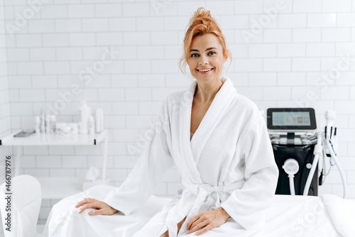 Portrait of pretty woman in soft bathrobe sitting on daybed after her beauty procedures. Female feeling satisfied and happy