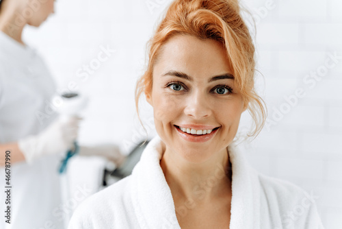 Young woman at beauty clinic cosmetology service sitting on medical chair and smiling to the camera. Skin care and treatment concept