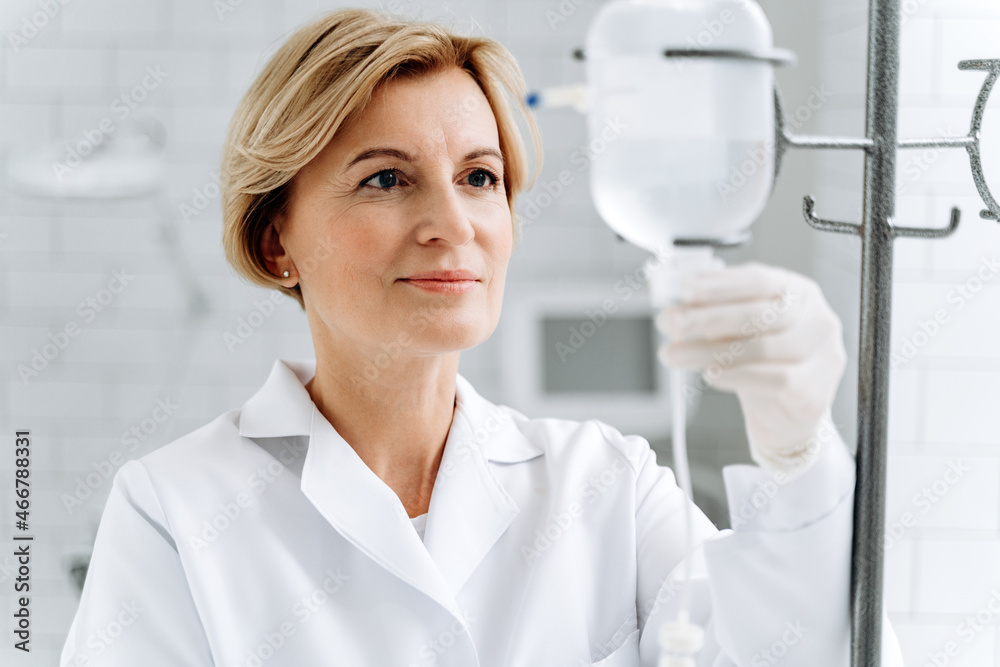 Concentrated senior female doctor is standing near the drop counter at the clinic. Medicine and healthcare concept