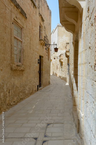 Typical Mdina street. Narrow medieval street of Mdina  also known as  Silent city   paved with stone slabs and surrounded with yellow limestone walls with vintage lanterns.