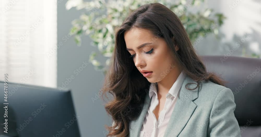 Beautiful secretary of company, assistant to boss, manager sits at desk in office in front of the computer screen, taps fingers on the keyboard, writes emails to clients, looks into the camera, smiles Beautiful secretary of company, assistant to boss, manager sits at desk in office in front of the computer screen, taps fingers on the keyboard, writes emails to clients, looks into the camera, smiles