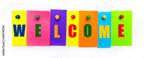 On a white background  buttons are used to fix bright multi-colored strips of paper with the text WELCOME