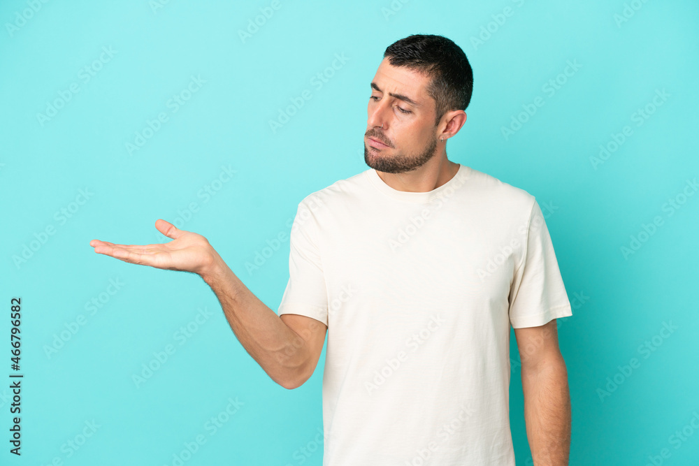 Young handsome caucasian man isolated on blue background holding copyspace with doubts Young handsome caucasian man isolated on blue background holding copyspace with doubts