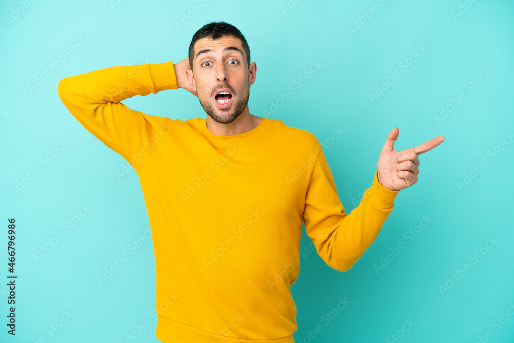 Young handsome caucasian man isolated on blue background surprised and pointing finger to the side Young handsome caucasian man isolated on blue background surprised and pointing finger to the side