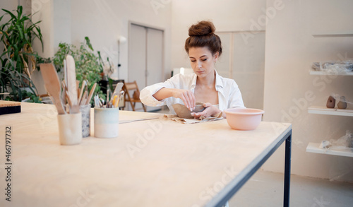 A woman ceramist hobbies working with clay, the manufacturing process. The sculptor makes handmade tableware. The master of ceramics is a professional doing business in the studio workplace.