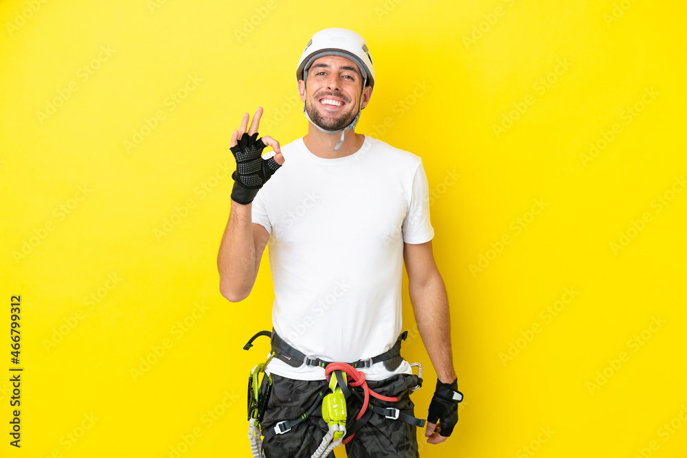 Young rock- climber man isolated on yellow background showing ok sign with fingers