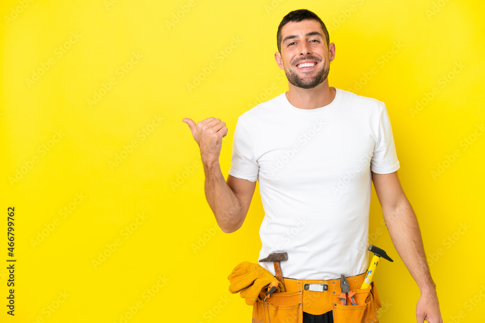 young electrician caucasian man isolated on yellow background pointing to the side to present a product - obrazy, fototapety, plakaty 