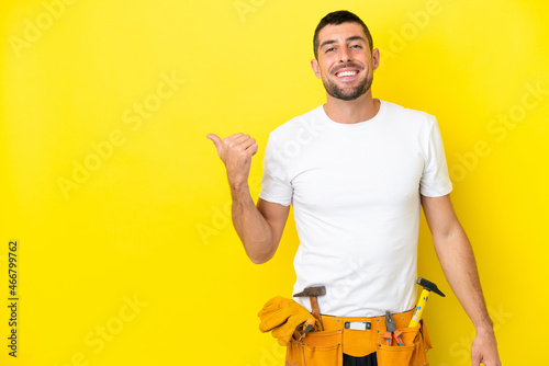 young electrician caucasian man isolated on yellow background pointing to the si Fotobehang