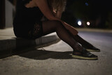 Drunk woman in dress sits on the roadside at night.