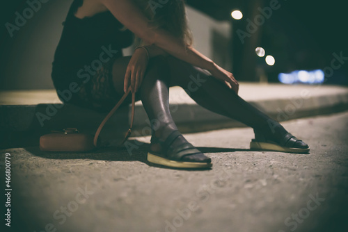 Drunk woman in dress sits on the roadside at night.