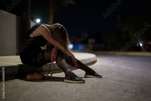 Drunk woman in dress sits on the roadside at night.