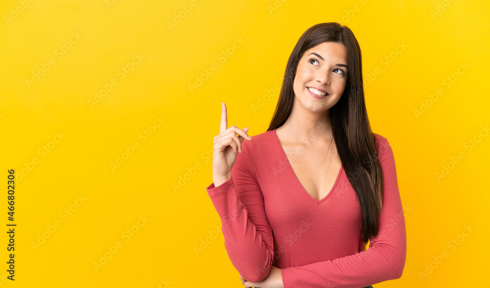 Teenager Brazilian girl over isolated yellow background pointing up a great idea Teenager Brazilian girl over isolated yellow background pointing up a great idea