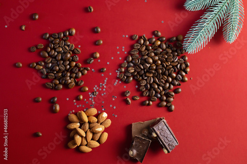 On a red background grains of coffee, chocolate, almonds and a spruce branch