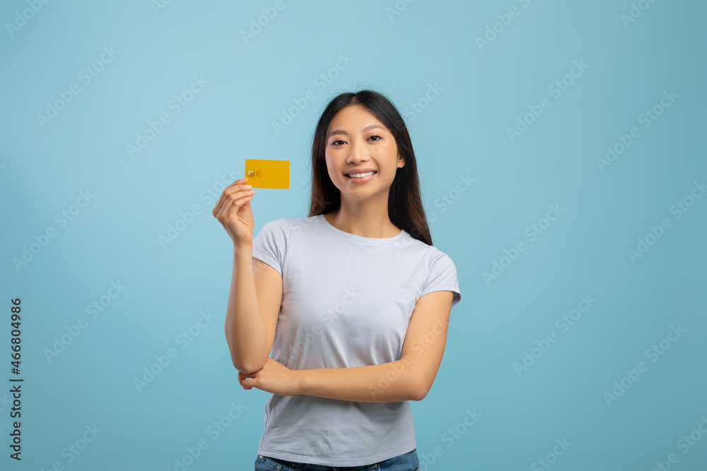 Easy payment concept. Happy young asian woman holding credit card in hand and smiling, standing over blue background Easy payment concept. Happy young asian woman holding credit card in hand and smiling, standing over blue background