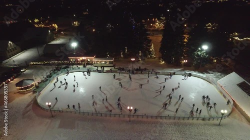 Aerial zooming shot of people skating in a beautiful ice rink at night. Drone zooms out an ice rink at night.