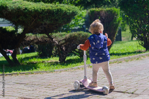 Blonde little girl driving or playing her scooter at the park with copy space 