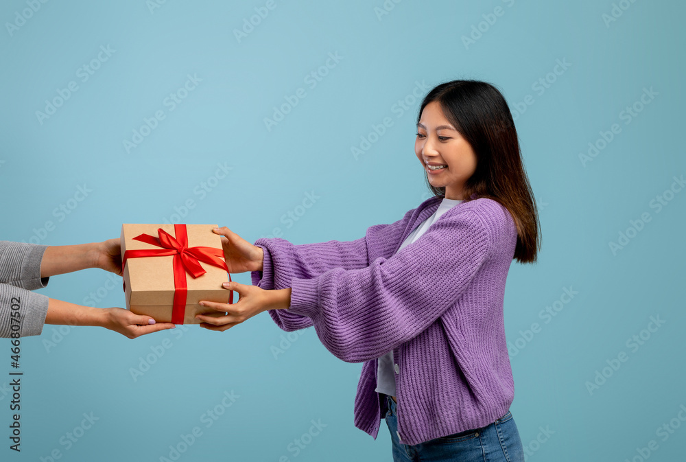 Happy asian lady receiving wrapped gift box, standing over blue studio background and smiling Happy asian lady receiving wrapped gift box, standing over blue studio background and smiling