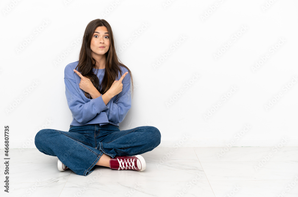 Young woman sitting on the floor pointing to the laterals having doubts