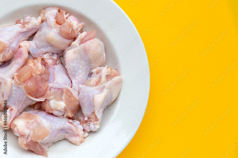 Fresh raw chicken wings (wingstick) in white plate on yellow background.