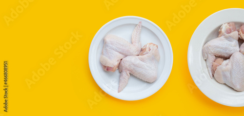 Fresh raw chicken wings in white dishes on yellow background.