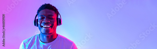Handsome young black man wearing headphones, listening to music with closed eyes in neon light, banner design photo