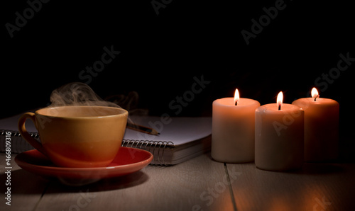 Cup of hot coffee with green smoke, books and burning candles. Desk table in power supply cut