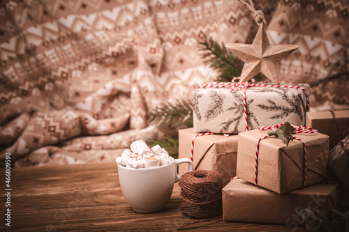 Pile of Christmas wrapped presents with twine string roll, fir tree branch, marshmallow cacao cup, Christmas toy star at wooden background. Xmas decoration, cozy festive composition, space for text