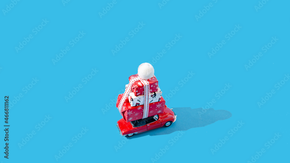 A red car with a pile of wrapped Christmas presents on the roof. Pastel blue background. Christmas or New Year celebration gifts creative concept. Card or banner or invitation design.