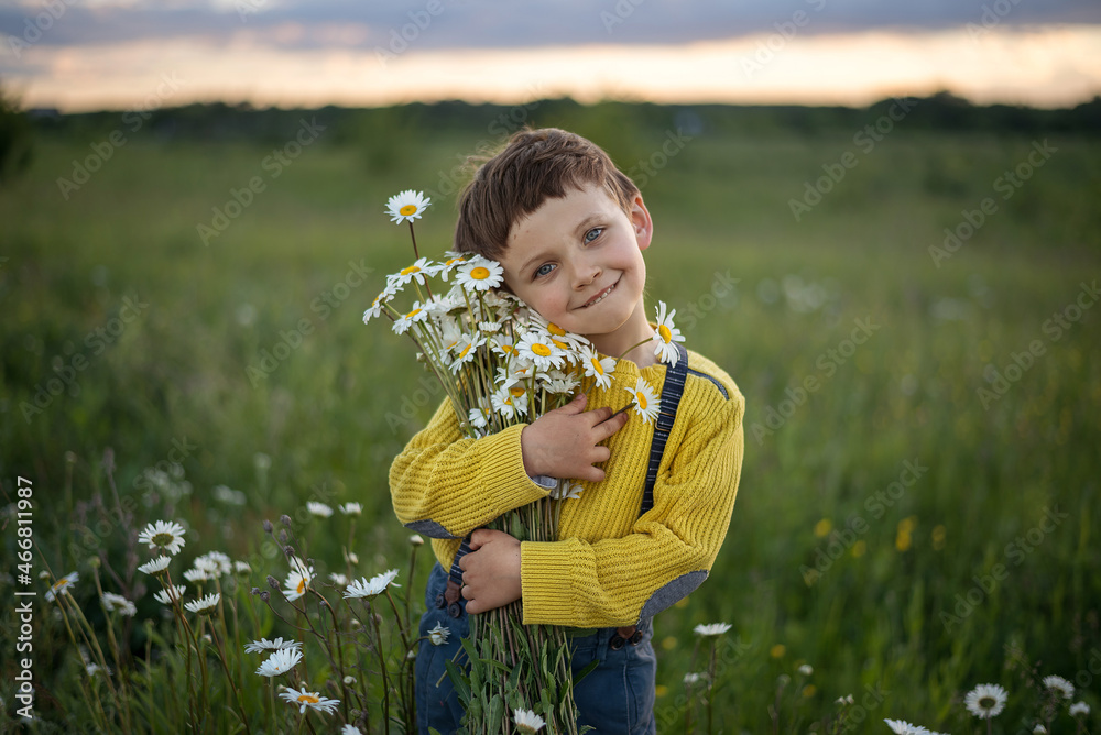 a boy in a yellow sweater and trousers with suspenders is standing in a meadow at sunset, hugging a bouquet of daisies a boy in a yellow sweater and trousers with suspenders is standing in a meadow at sunset, hugging a bouquet of daisies