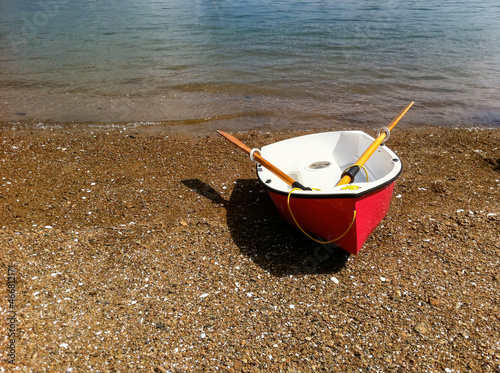 Red dinghy, with yellow oars on a deserted pebble beach, summer, Mansion House Bay, Kawau Island, New Zealand photo