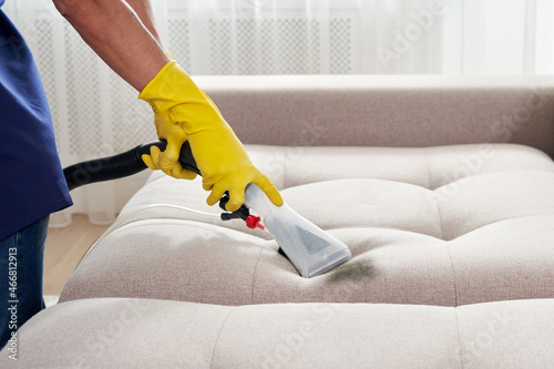 Close-up of housekeeper holding modern washing vacuum cleaner and cleaning dirty sofa with stain with professionally detergent. Professional springclean at home concept photo